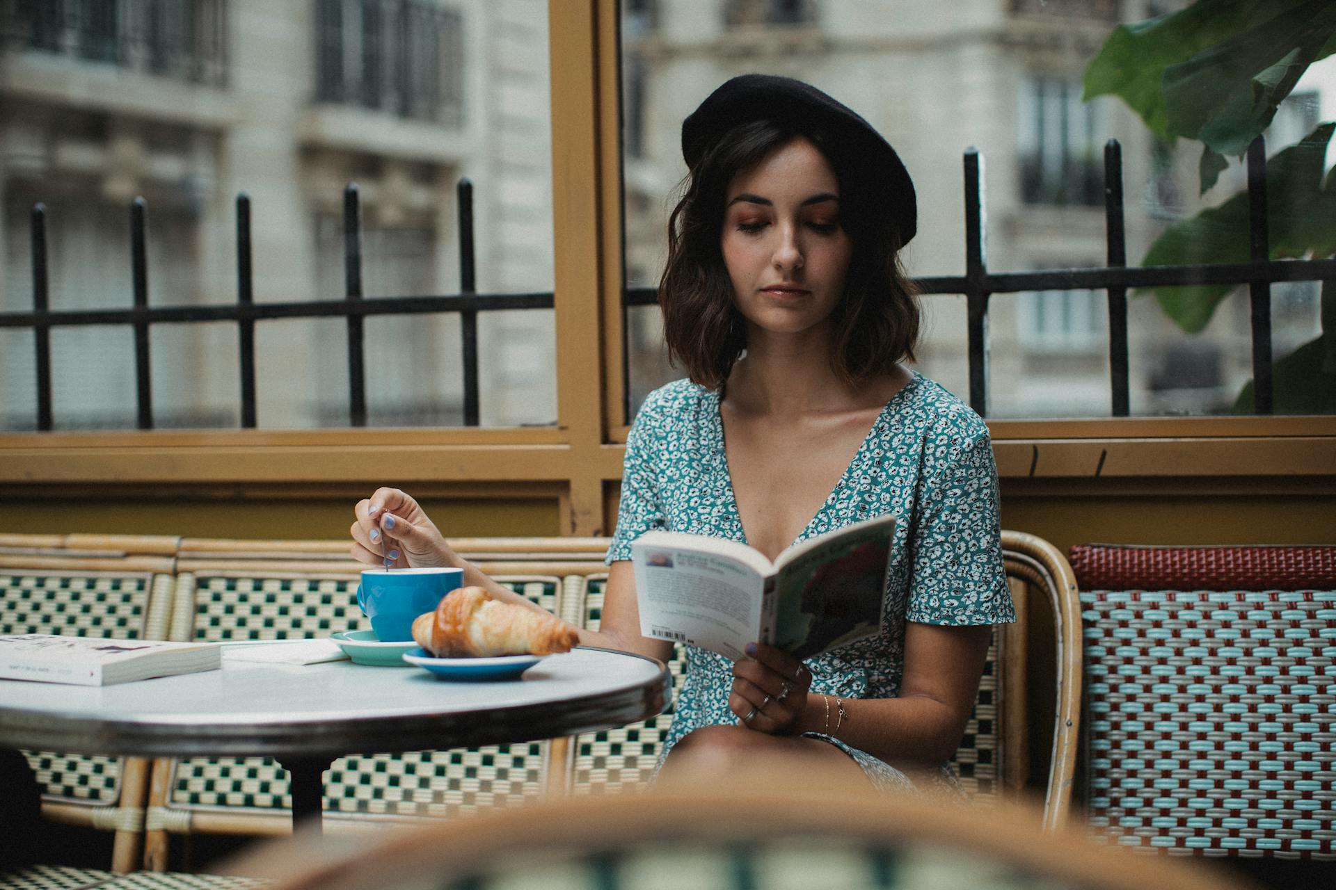 Woman in Blue and White Floral Dress Sitting on a Chair While Reading