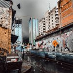 Person Walking On A Wet Street Along A Building With Mural Under Gray Sky in Bogotá, Colombia