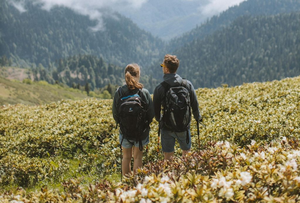 Couple in Black Jacket and Black Backpack Standing on Green Grass Field