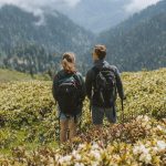 Couple in Black Jacket and Black Backpack Standing on Green Grass Field