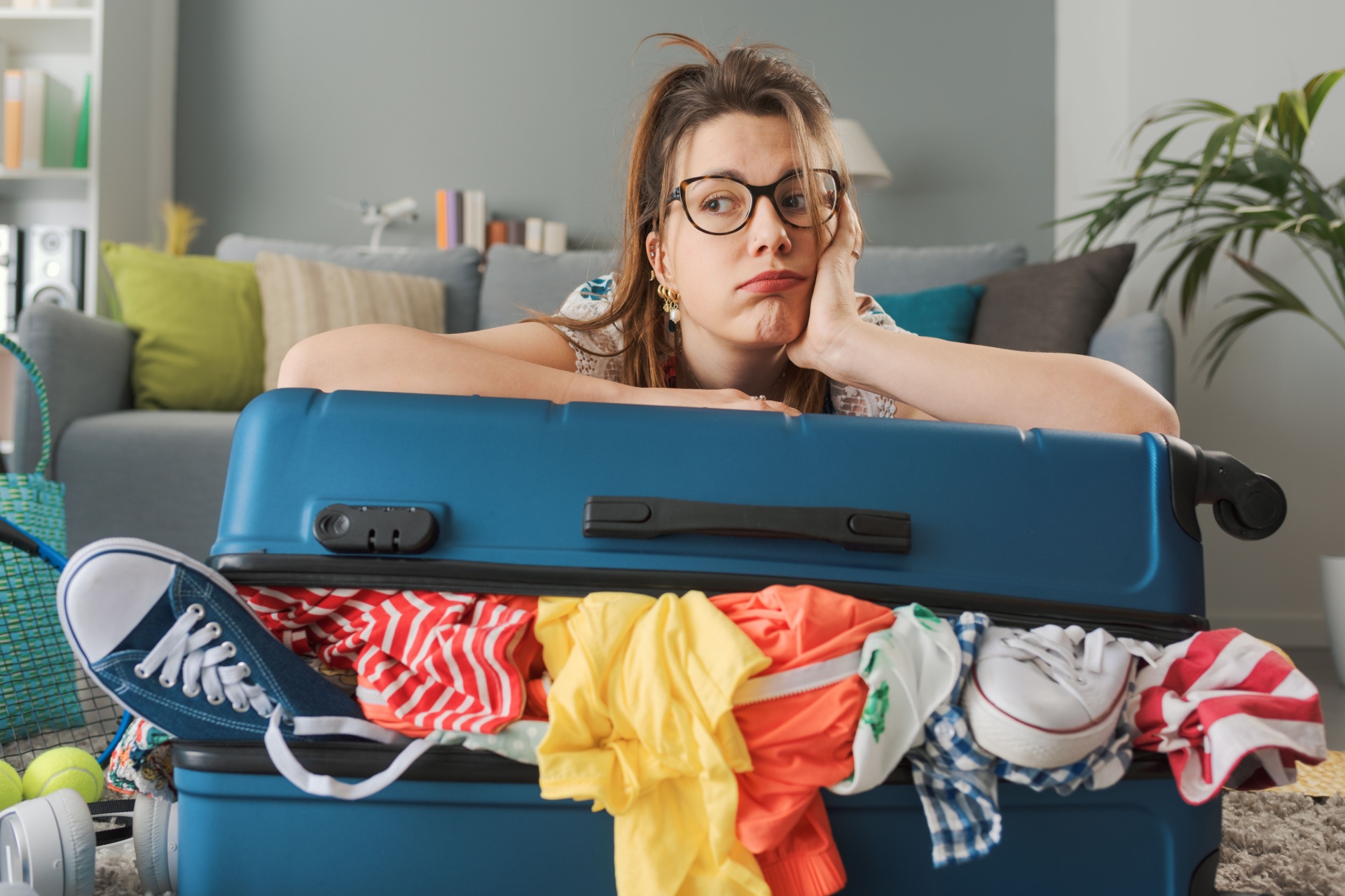 Tired sad woman packing for a long journey, she is leaning on her overfilled trolley bag: travel, vacations and tourism concept
