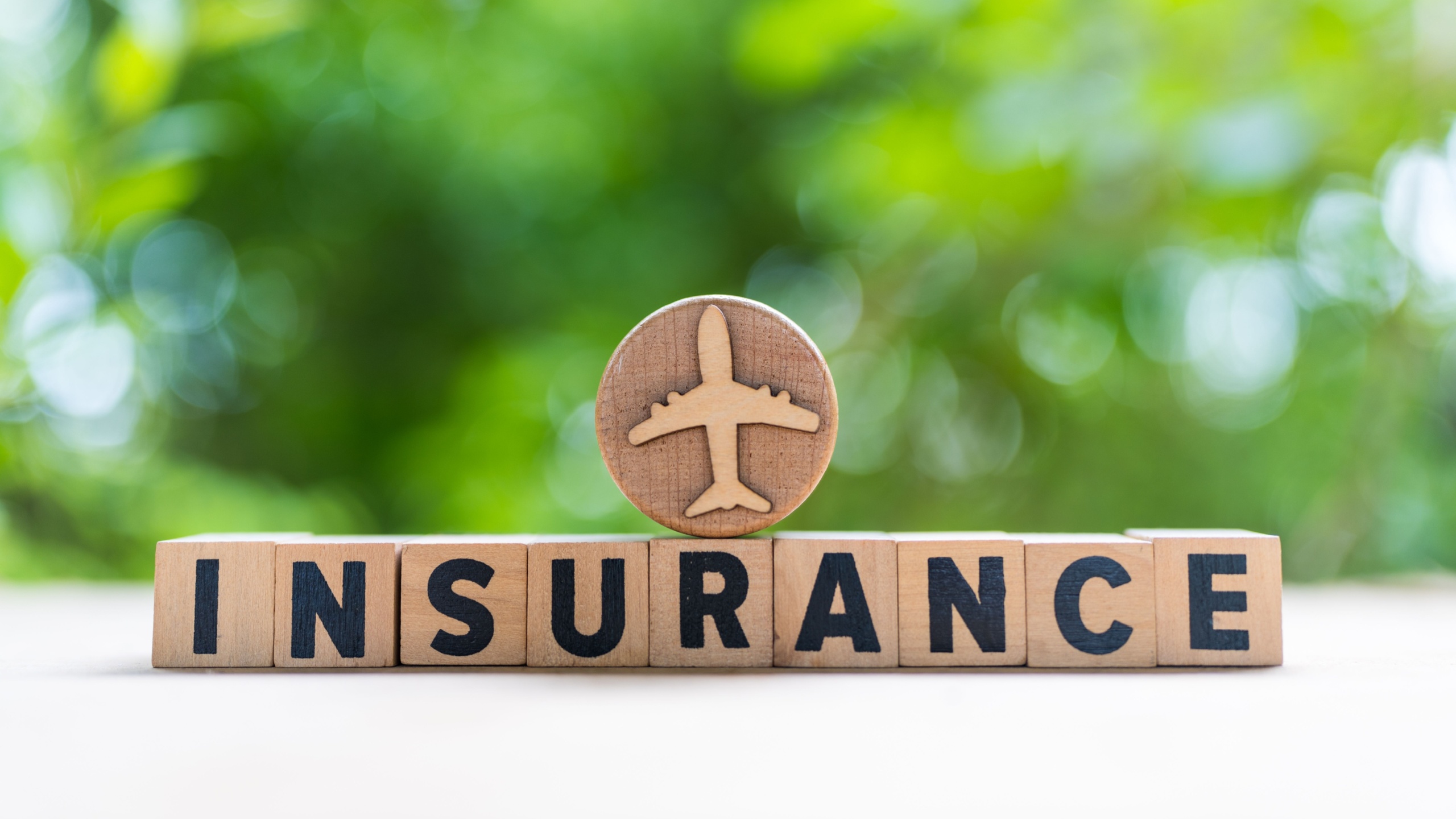 Insurance word on wooden block and symbol with airplane on a blurred nature background, concept of travel insurance and travel insurance.