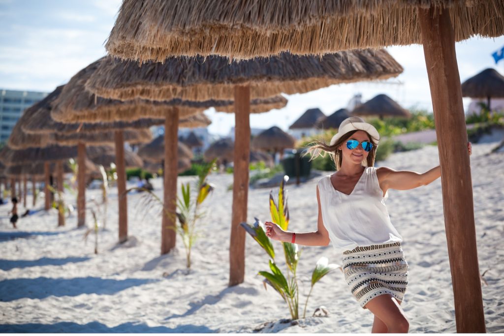 Beautiful tanned woman posing in sunshade under beach palapa, enjoying summer vacation