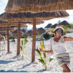 Beautiful tanned woman posing in sunshade under beach palapa, enjoying summer vacation