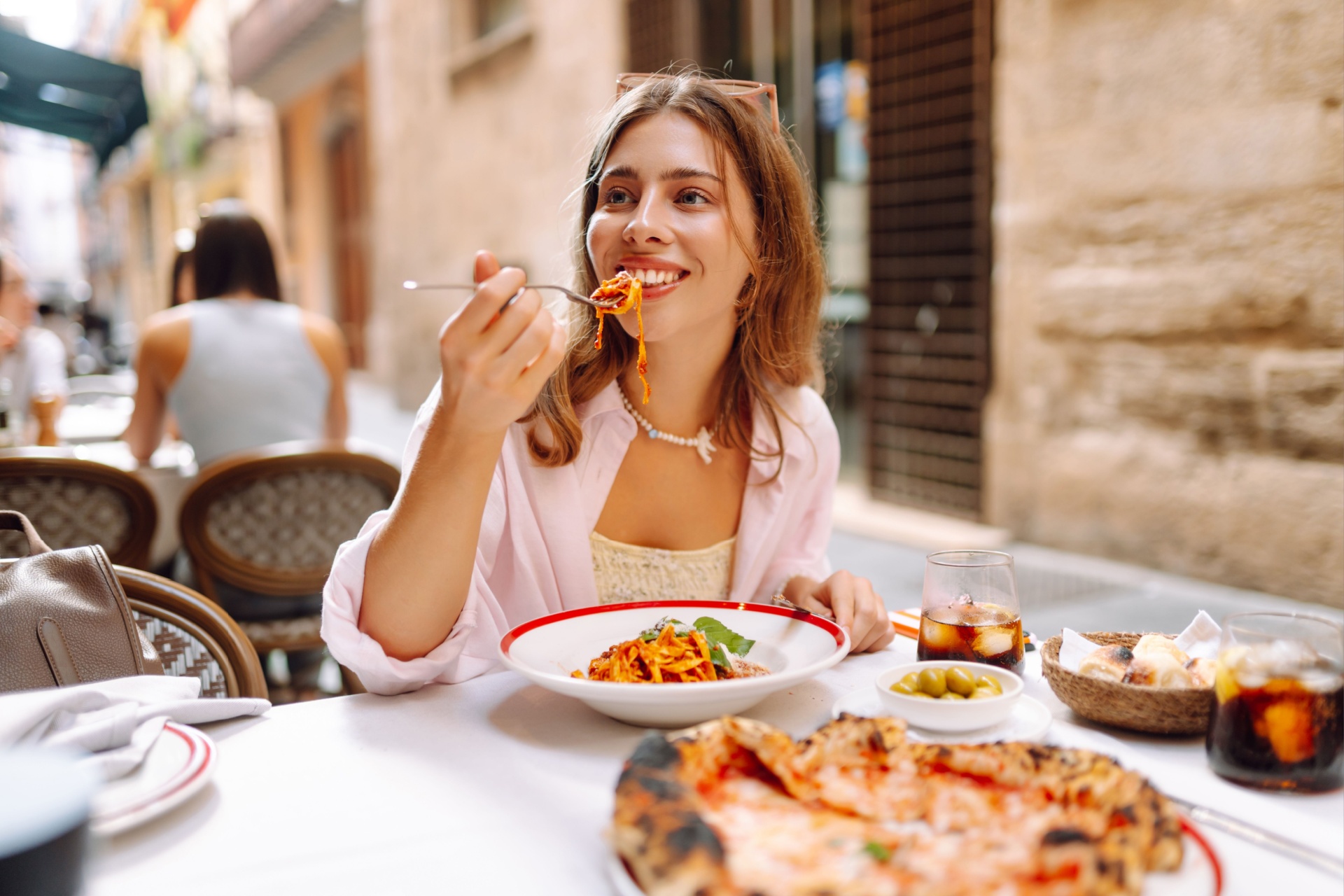 A happy woman eats fresh Italian pasta at a cafe table. A young tourist enjoys spaghetti on a sunny day on the terrace. Concept of food, enjoyment.