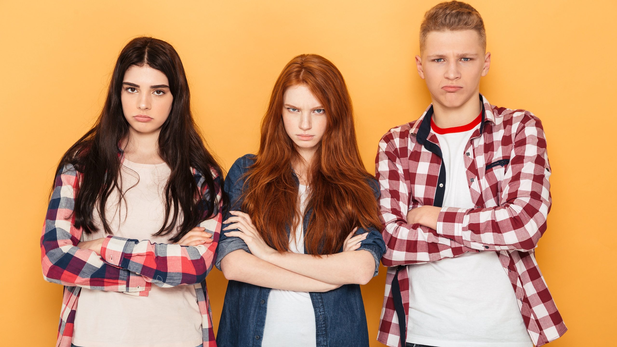 Group of upset school friends looking at camera while standing together over yellow background