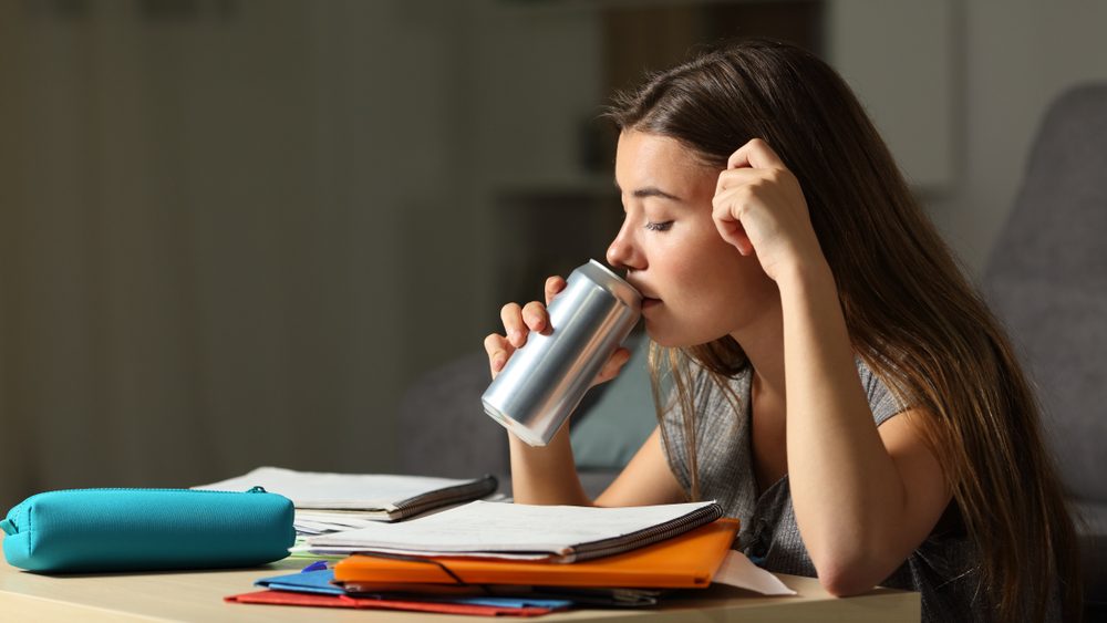 Studious teen studying drinking energy beverage while is studying in the night at home