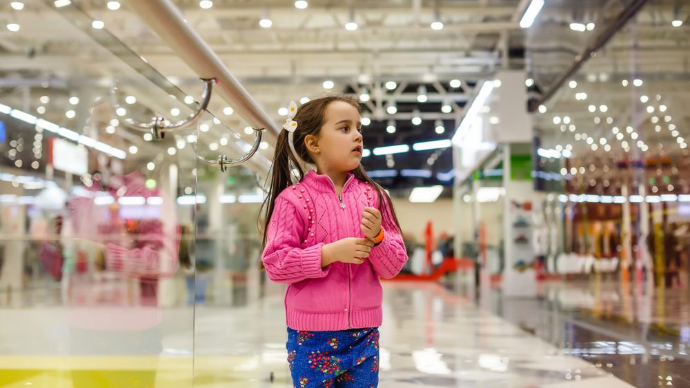 Little girl alone in shopping mall center, looking for her mother. The child was lost in the big store.