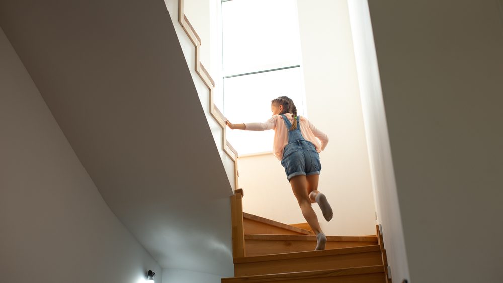 Back view of adorable female child in denim overalls running upstairs
