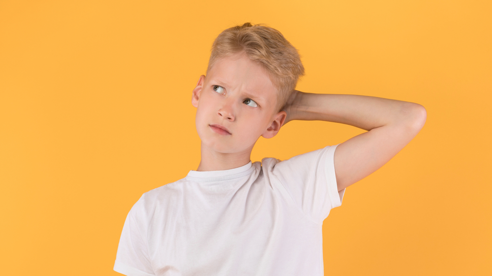 Question Concept. Headshot of puzzled boy scratching head looking up over pastel orange studio wall