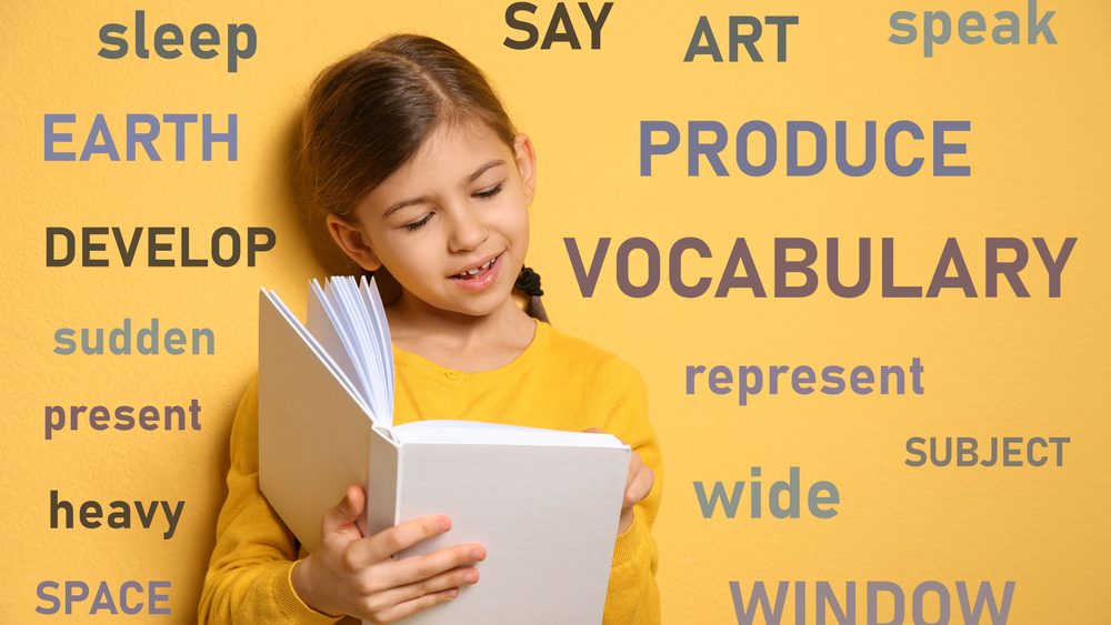 Cute little girl reading vocabulary surrounded by different words in English on yellow background