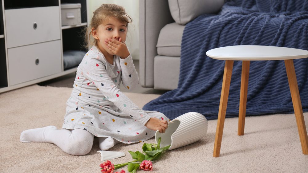 Emotional little girl and broken ceramic vase on floor at home