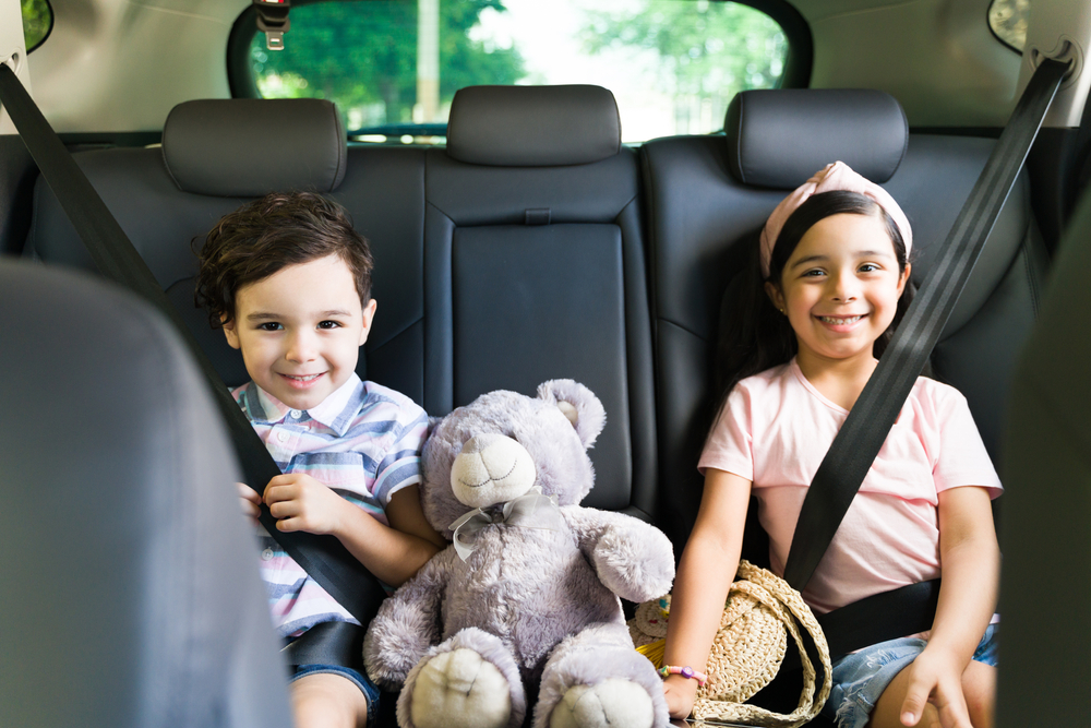 Well-behaved kids sitting in the car. Portrait of an adorable little brother and sister smiling while waiting for their parents with their seat belt on 