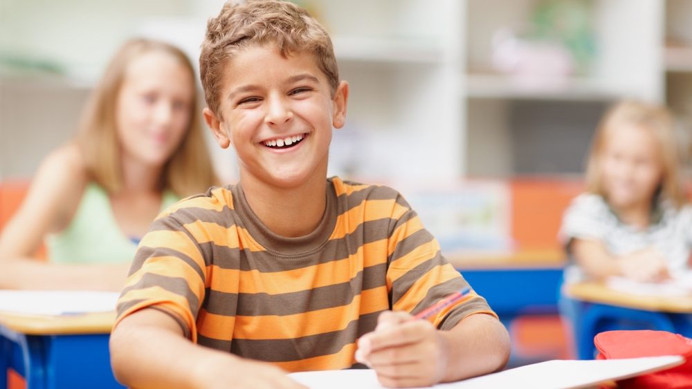 Enjoying a lighthearted moment in class. Sweet schoolboy sitting at his desk in class laughing happily.