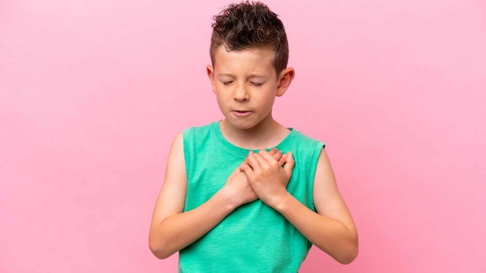 Little caucasian boy isolated on pink background having a pain in the heart