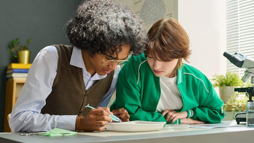 Two teenage intercultural students of highschool doing dissection of frog at lesson while one of them using tweezers to take animal