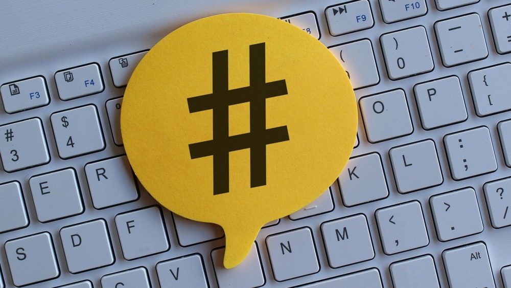 Top view image of computer keyboard and speech bubble with hashtag icon.