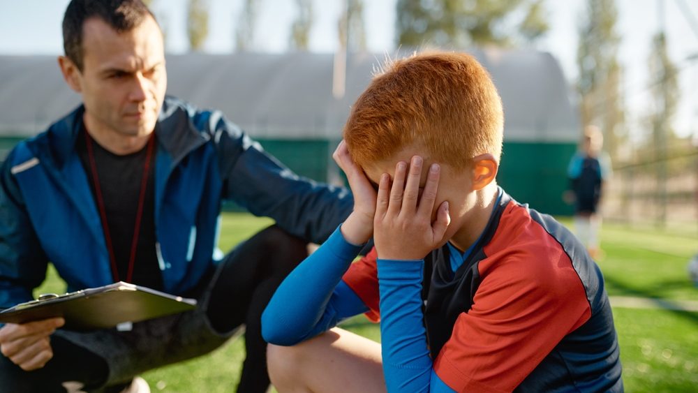 Coach comforting crying little soccer player after missed goal