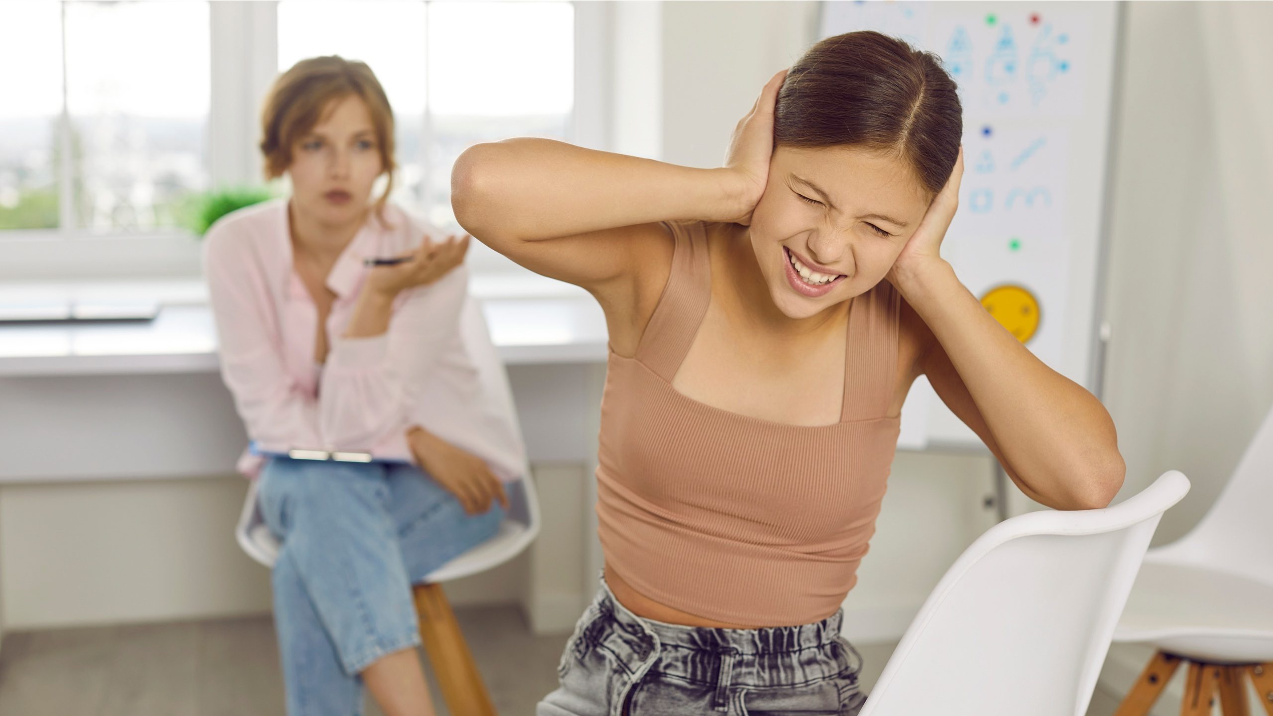 Problem child at interview meeting at psychologist office. Disobedient bad tempered rude angry adolescent teenage girl covers, closes ears with hands ignoring therapist's professional help and support