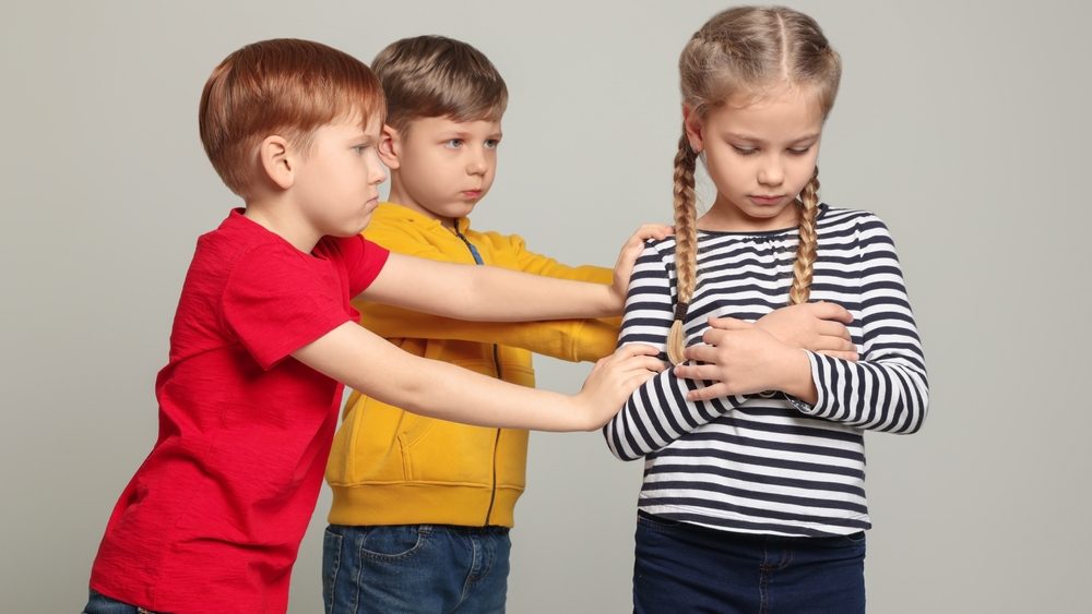 Boys bullying girl on light grey background