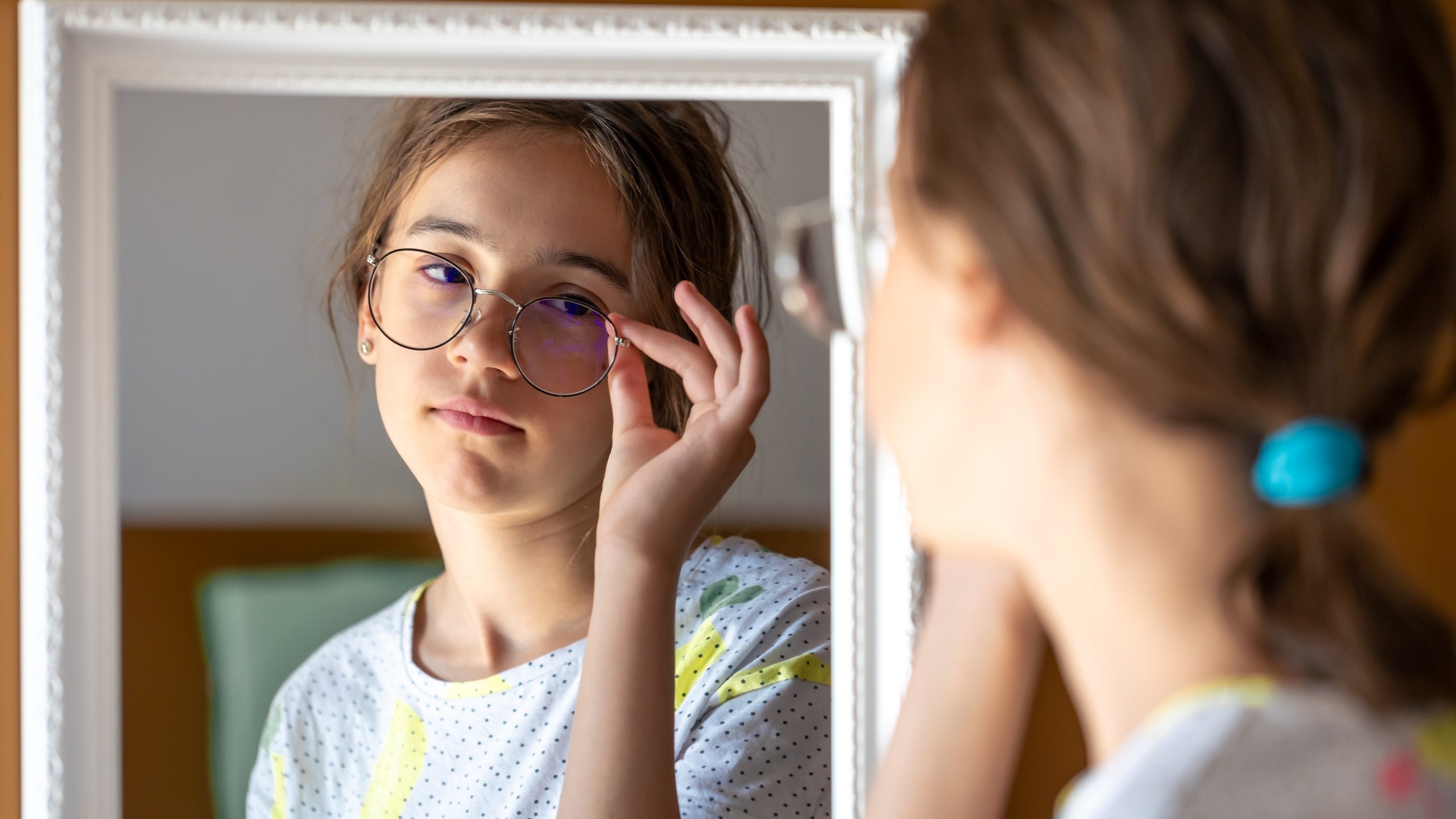 A teenage girl looks at herself in the mirror in the morning.