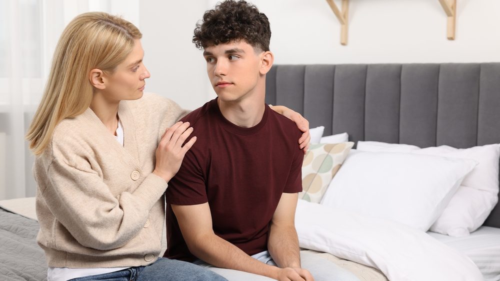 Mother consoling her upset son in bedroom, space for text. Teenager problems
