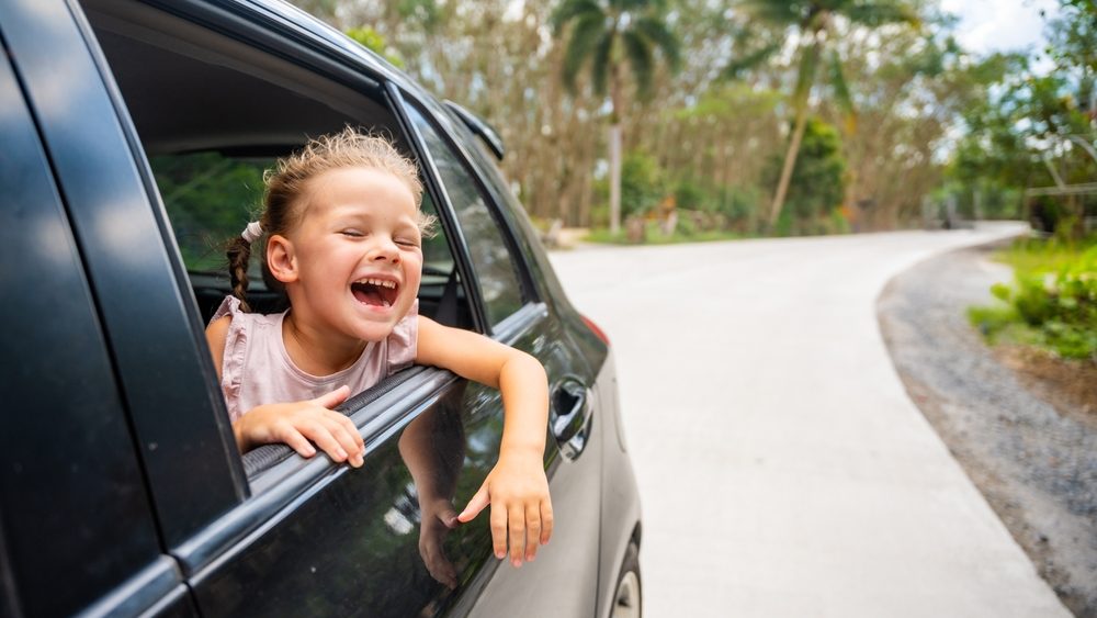 Happy little girl peeking out of window of the car during traveling, family trips by car with children concept. High quality photo