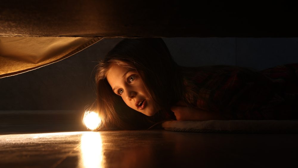 Little girl with flashlight looking for monster under bed at night
