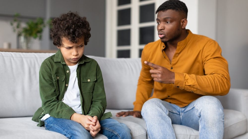 A father seems to be giving his son a serious talk, with the child looking down and the dad pointing a finger