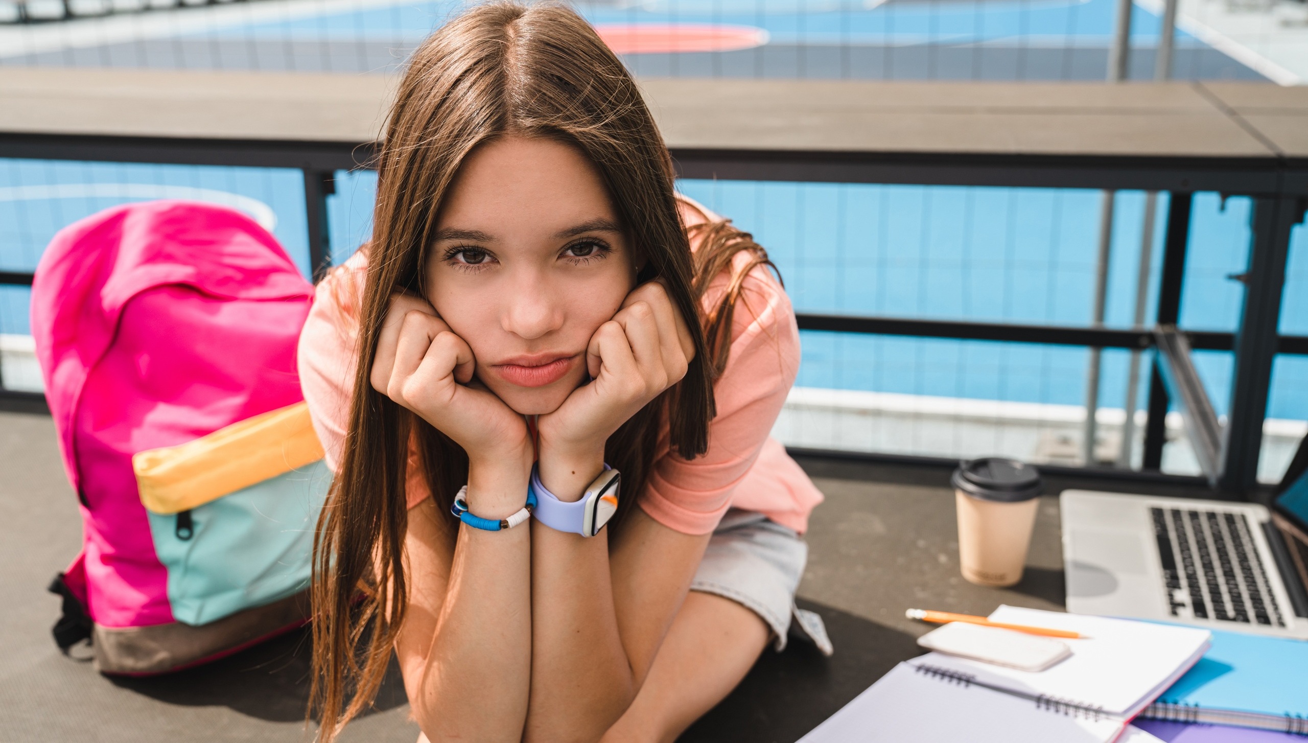 Sad sorrowful high school girl teenager pupil college student in casual clothes with bag using laptop doing home work task sitting alone in sport yard basketball court copy space. Education concept