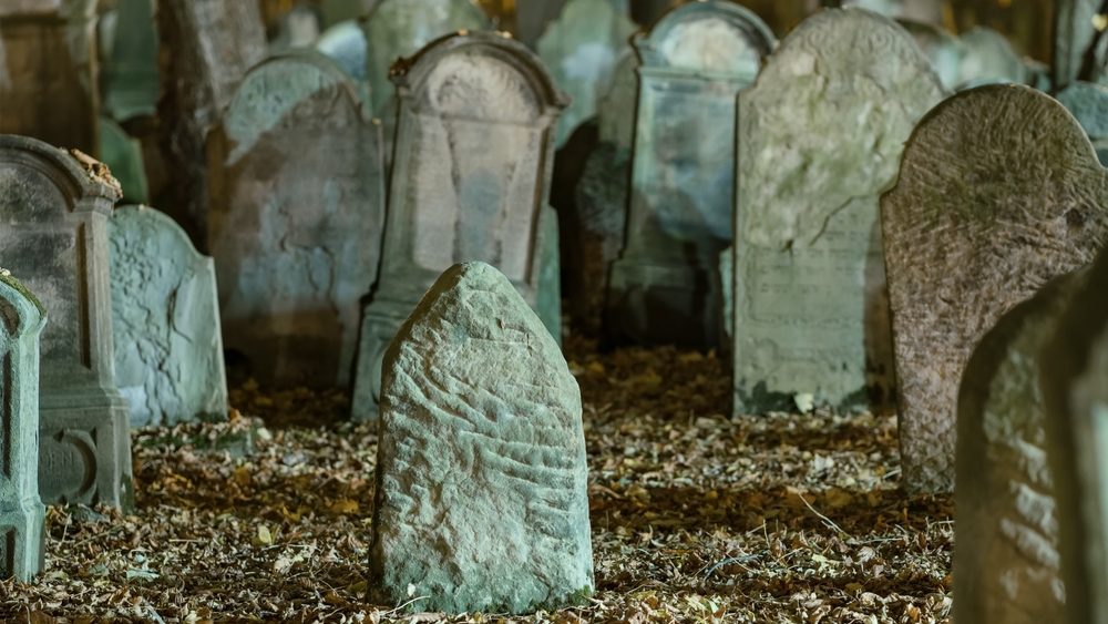 Tombstones in an old cemetery at night. Blanketed gravestones create a spooky scene. Leaning tombstones add to the eerie ambience in a dark autumn setting. Creepy aged tombstones in the graveyard.