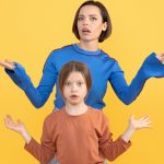 A mother and her preteen daughter display a moment of shared confusion and surprise against a bright yellow background. They both express emotions of bewilderment together.