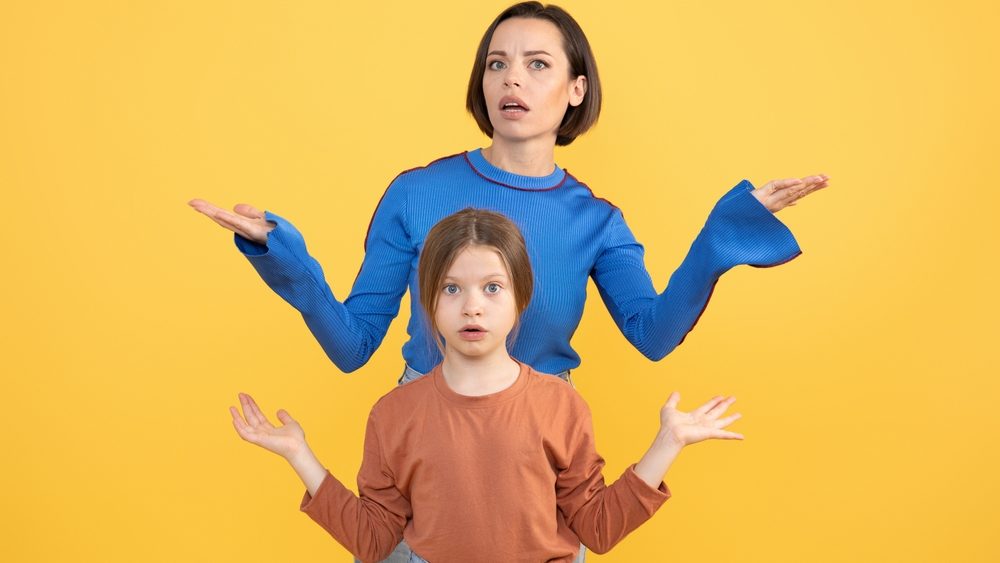 A mother and her preteen daughter display a moment of shared confusion and surprise against a bright yellow background. They both express emotions of bewilderment together.