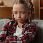 Portrait at home serious sad upset frustrated offended lonely Caucasian little girl female daughter adopt custody child kid teenager at couch problem domestic violence boring family trouble bad mood