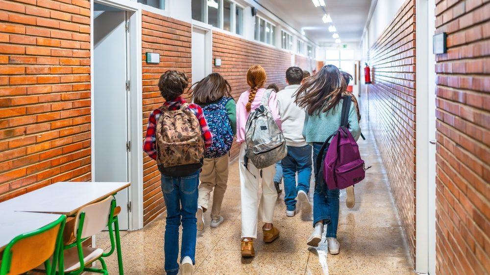 Rear view of elementary school students running down school hallway between classes, carrying backpacks