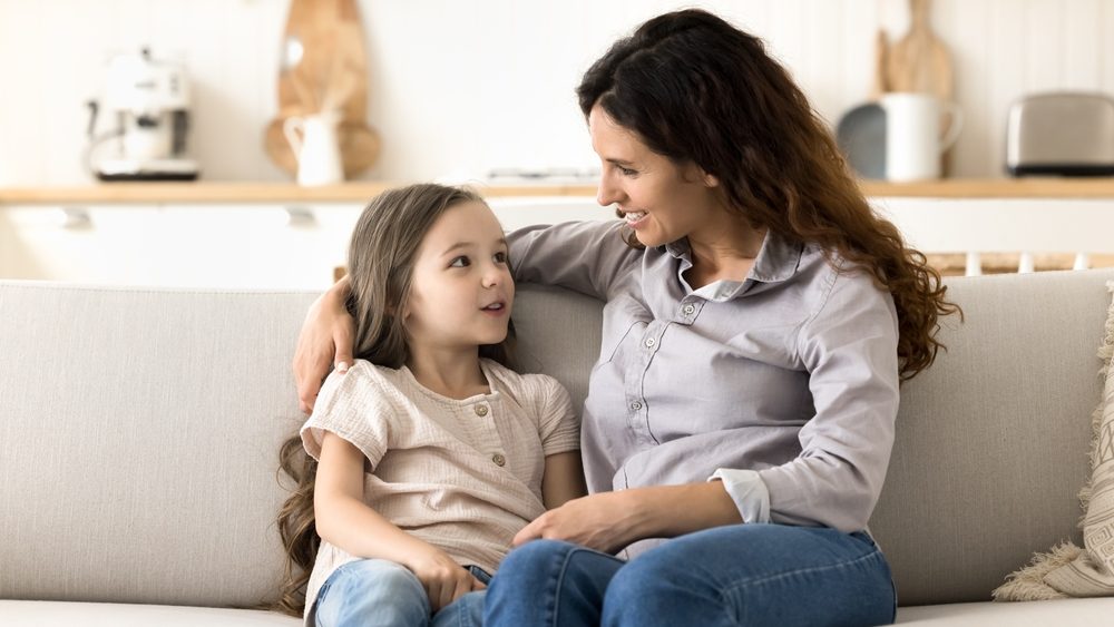 Talking to mom. Attentive caring foster mother spend quality time with beloved little daughter hug chat hold conversation share news enjoy trusted communication with adopted kid sitting on comfy sofa