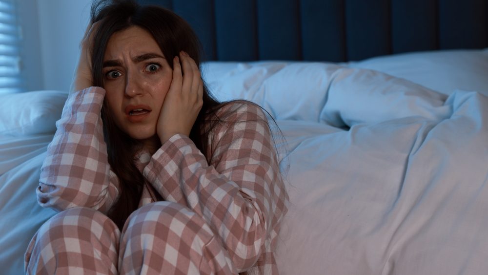 Fear of darkness. Scared young woman in bedroom at night, space for text