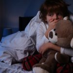 Scared boy with teddy bear in bed at night. Space for text