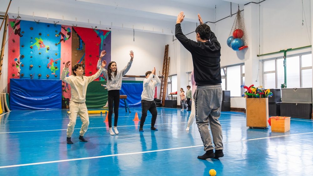 Students jumping and raising their arms, following their gym teacher's instructions during a physical education class