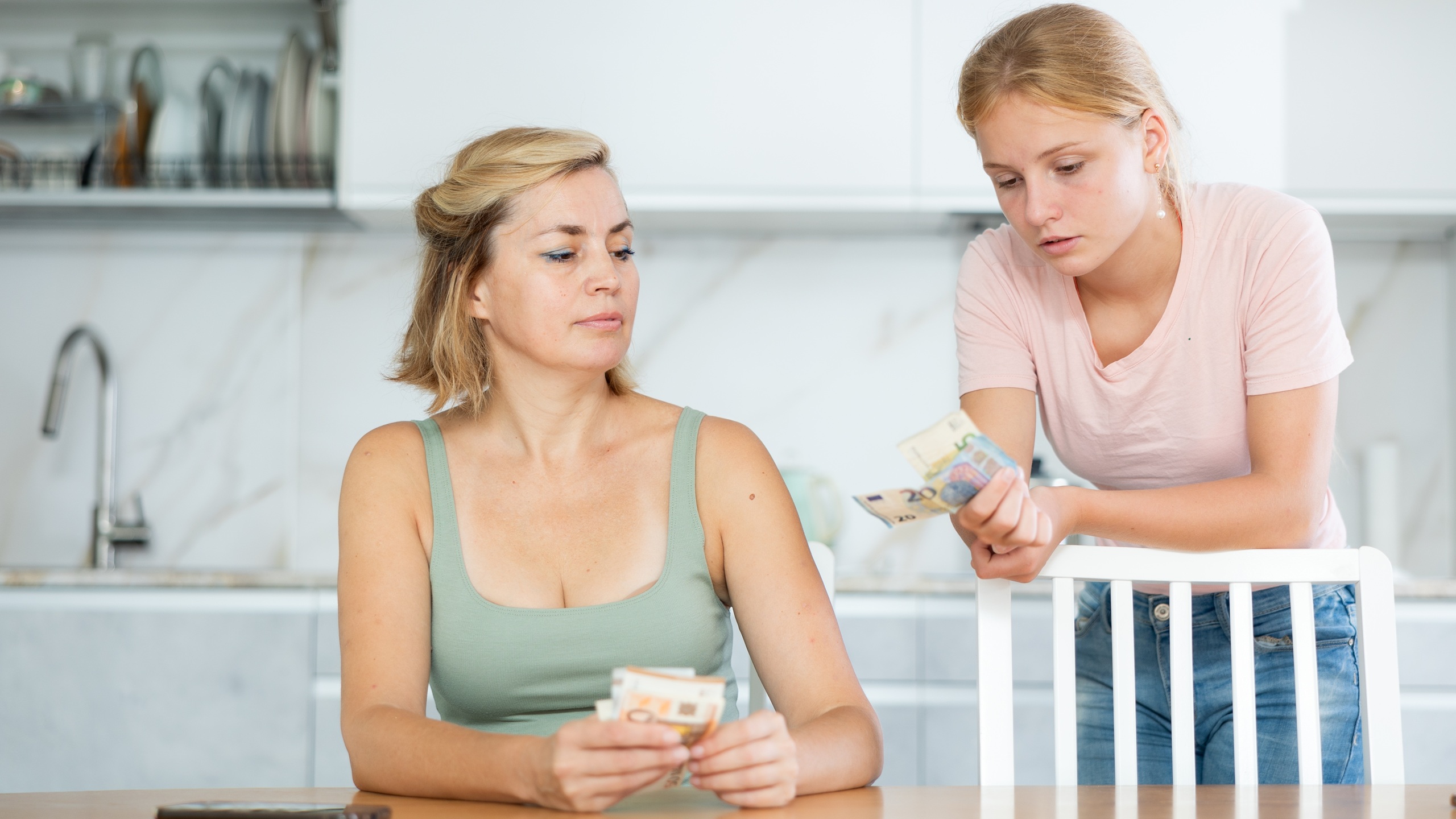 Middle-aged woman gives money to teenage girl for doing household chores. Girl earns extra money during school holidays