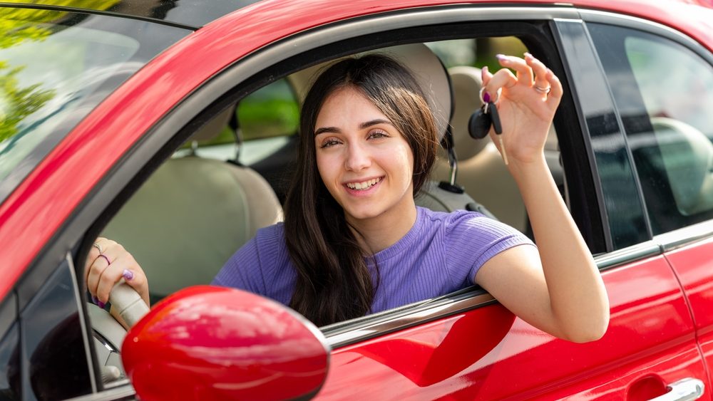 Happy young woman showing car keys while driving a red car