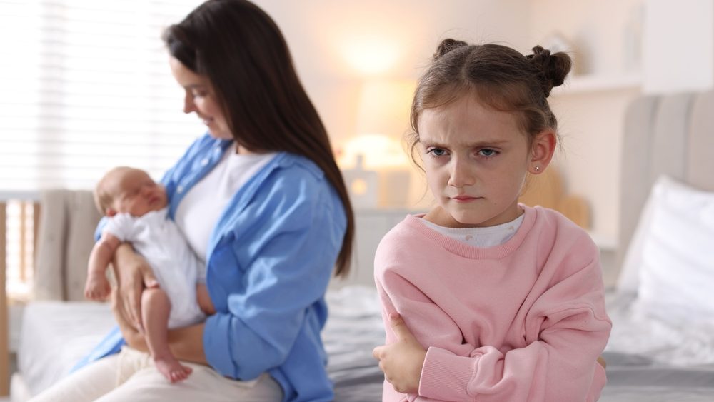 Jealous little girl upset about mom spending time with newborn baby at home, selective focus