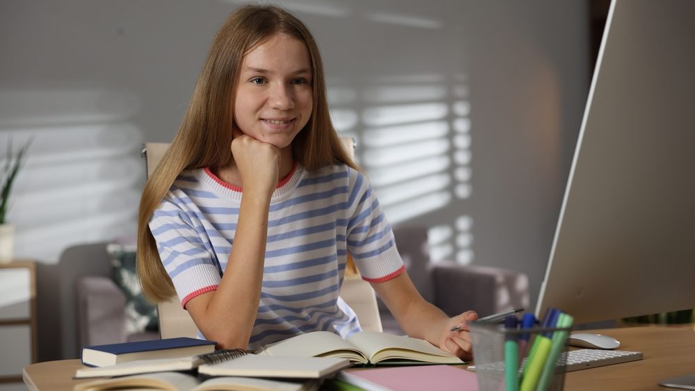 Teenage girl studying online at table indoors
