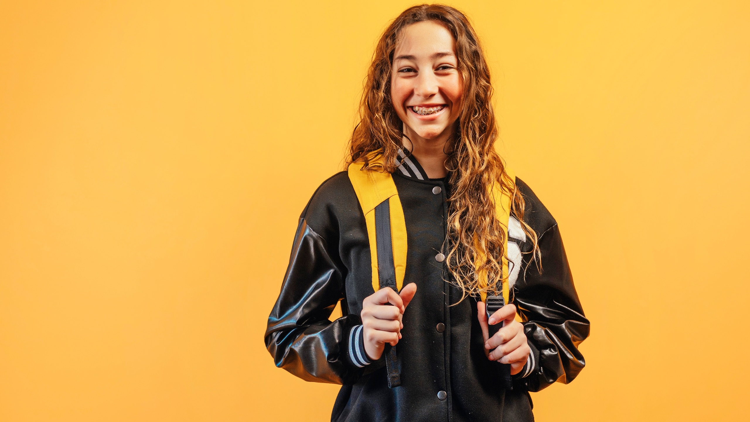 Teen girl smiling with backpack, orange background.