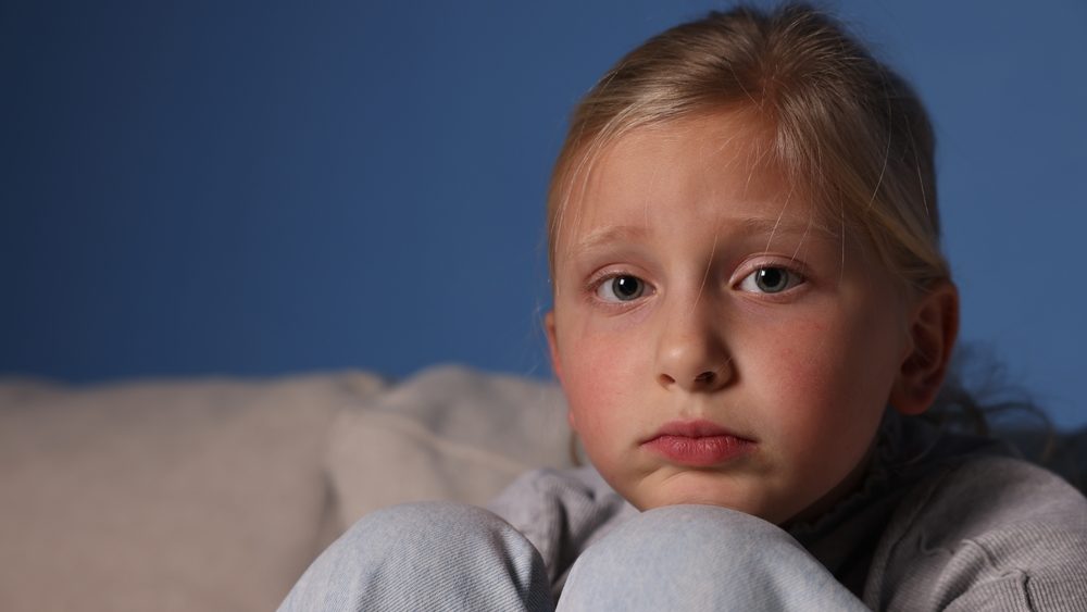 Sad little girl on sofa indoors, space for text
