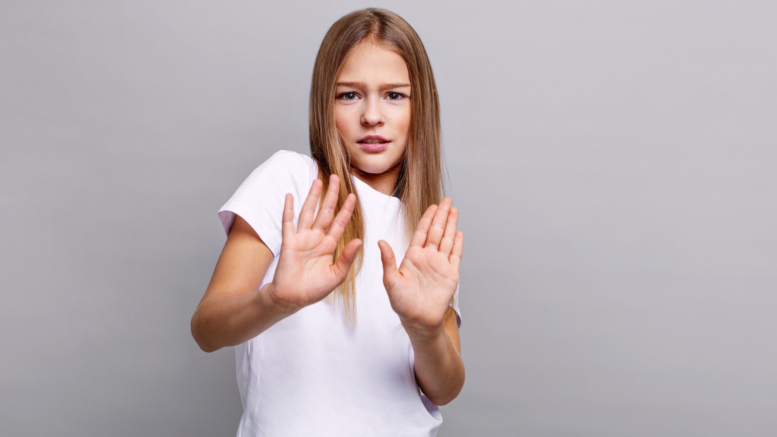 Portrait preteen girl child making stop gesture with hands, looking serious and cautious, standing in studio, expressing refusal, boundaries, disagreement and safety awareness, kids emotions