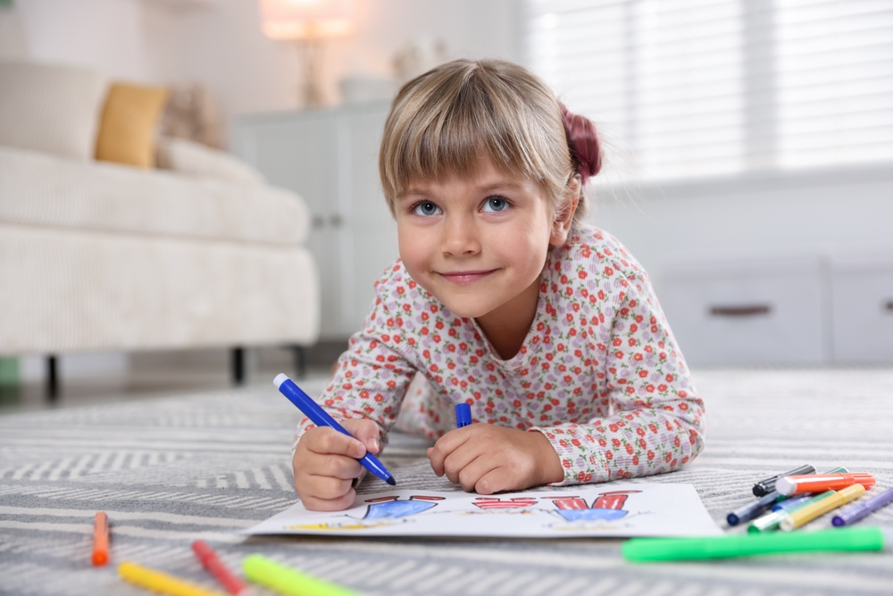 Cute little girl drawing with felt pen on floor at home, space for text
