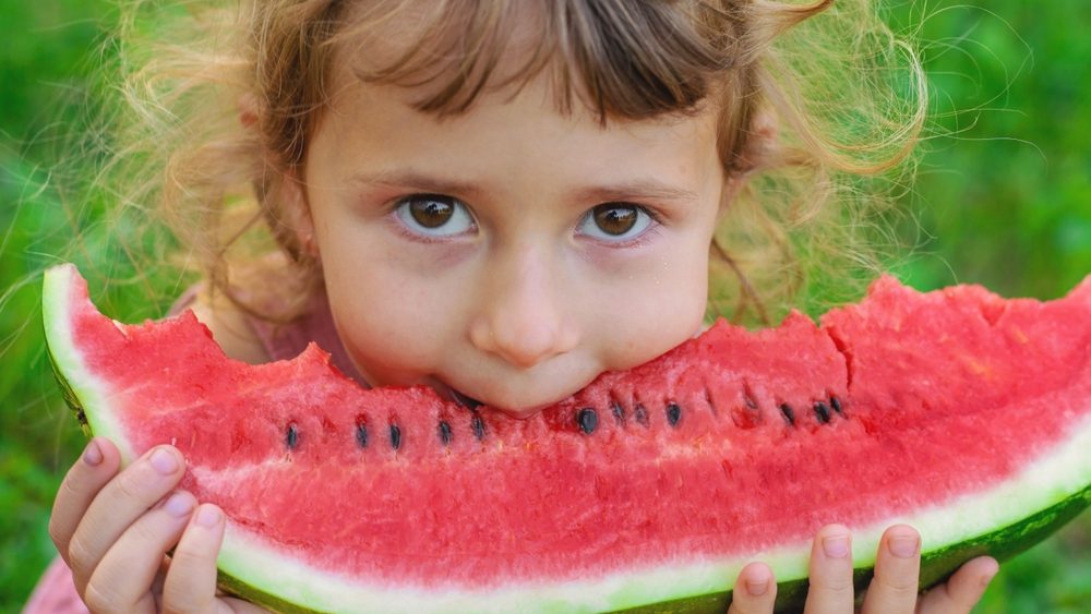 A child eats an watermelon in the park. Selective focus. Kid.