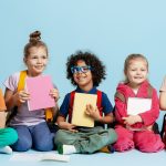 Group of multiethnic kids smiling, sitting on a blue background, prepared to learn at school