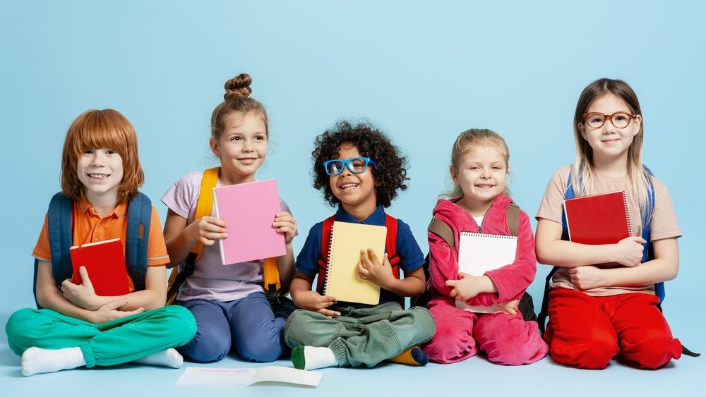 Group of multiethnic kids smiling, sitting on a blue background, prepared to learn at school
